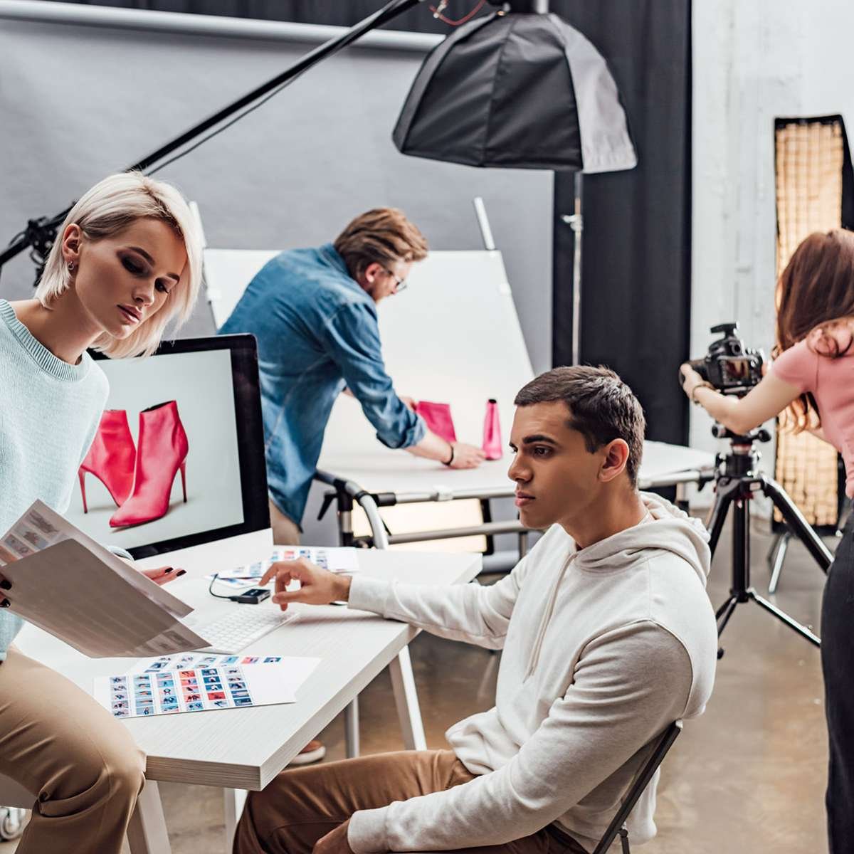 attractive art director looking at photos near computer monitor and assistant