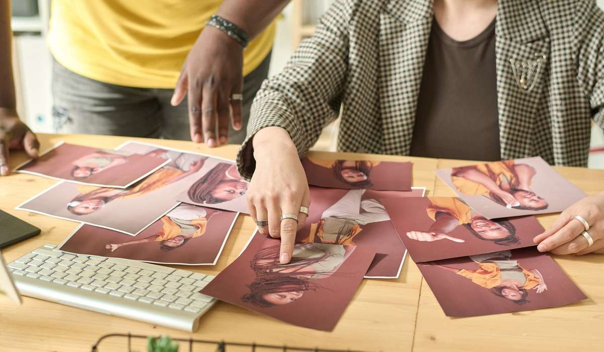 Close-up of designer pointing at photo sitting at table, she choosing photos together with editor for content